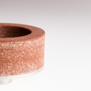 Close-up of cylindrical grinding wheel with textured abrasive surface mounted on white base, designed for precision metalworking and industrial surface finishing