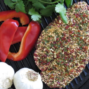 Leonards Gluten Free Pepper Steak Coater 2kg Tub seasoning applied to steak with garlic, red bell peppers, and fresh herbs on a grill pan
