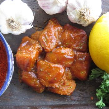 Raw chicken pieces glazed with Leonards Gluten Free Tikka Masala, presented with ingredients including garlic, lemon, and paprika, a product from Parkers Food Machinery Plus.