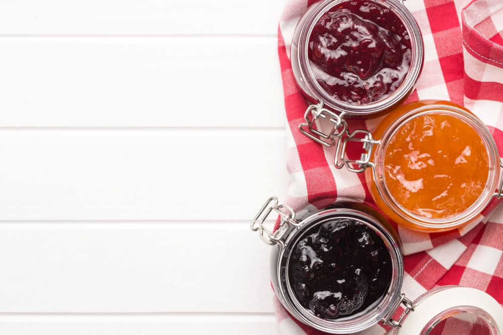 Three open glass jars of assorted jam