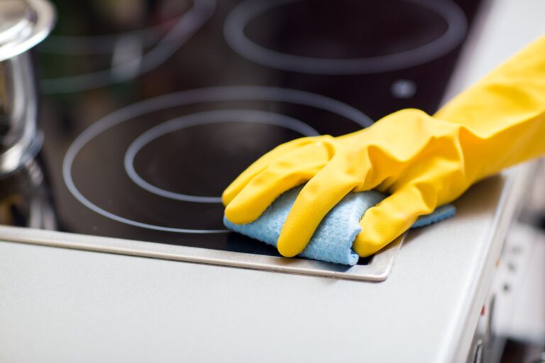 Close-up of stovetop cleaning with yellow gloves and blue cloth on a black glass-ceramic surface – Parkers Food Machinery Plus kitchen cleaning products