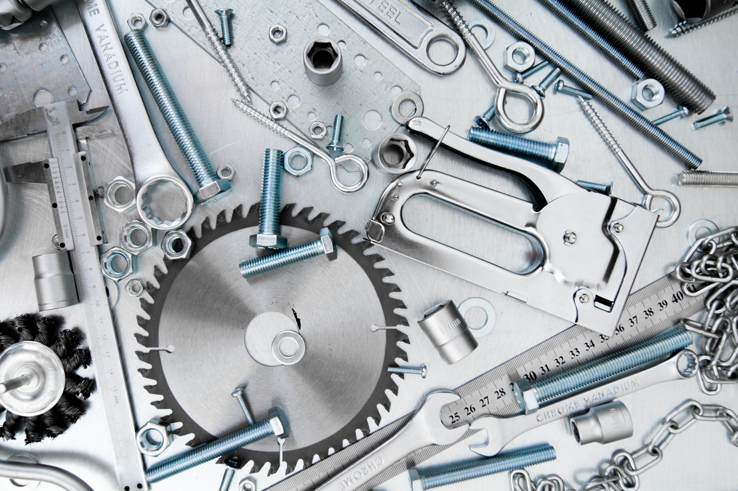 Assorted metal spare parts scaled and tools for industrial food machinery, including saw blades, wrenches, calipers, and fasteners on a metallic surface