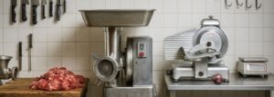 Professional butcher’s workspace with meat grinder, slicer, and knives displayed on tiled wall, showcasing essential butchers’ equipment.