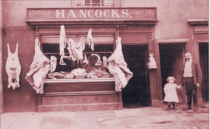 Alt text: Historic photo of Hancocks Butchers in Monmouth with family and traditional meat display, representing over a century of local craftsmanship at PFM Plus.