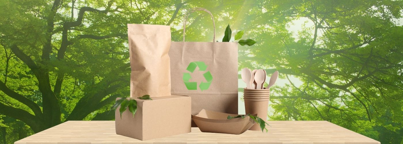 Eco-friendly packaging products made from recyclable paper and cardboard displayed on a wooden table against a green forest background.